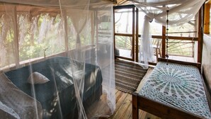 Quarto com uma cama coberta por um mosquiteiro, um banco de madeira e vista para o exterior.