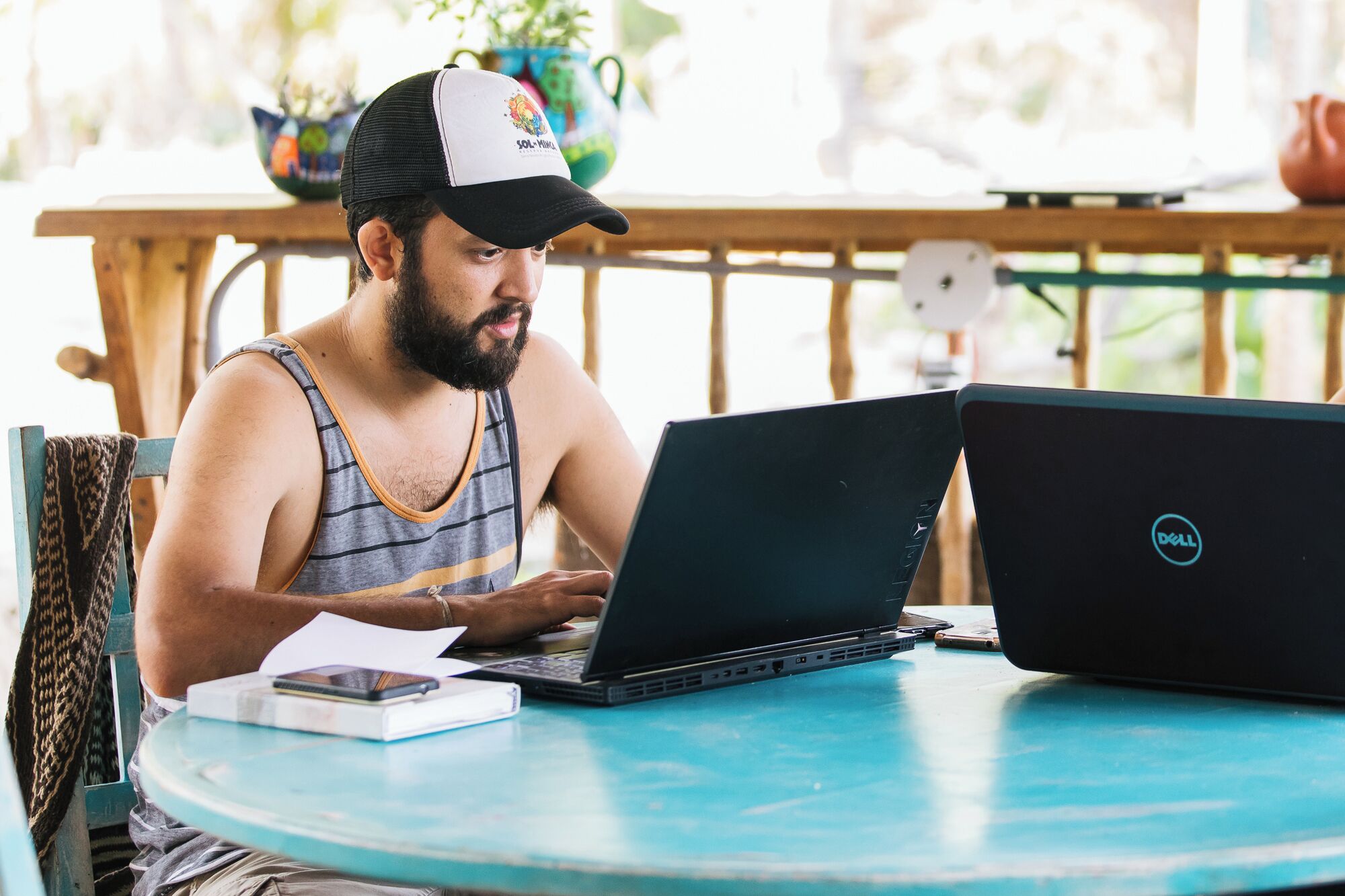 A person sitting at a round table with two laptops, one with a Dell logo, and a smartphone on the table.
