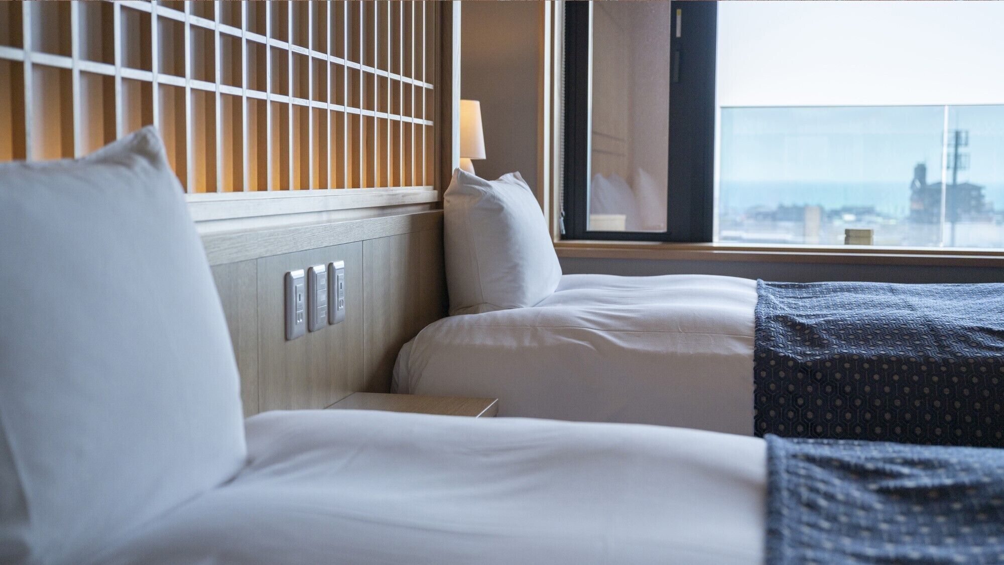 Habitació d'hotel amb dos llits, una finestra amb vista a la ciutat i una paret amb un llum.