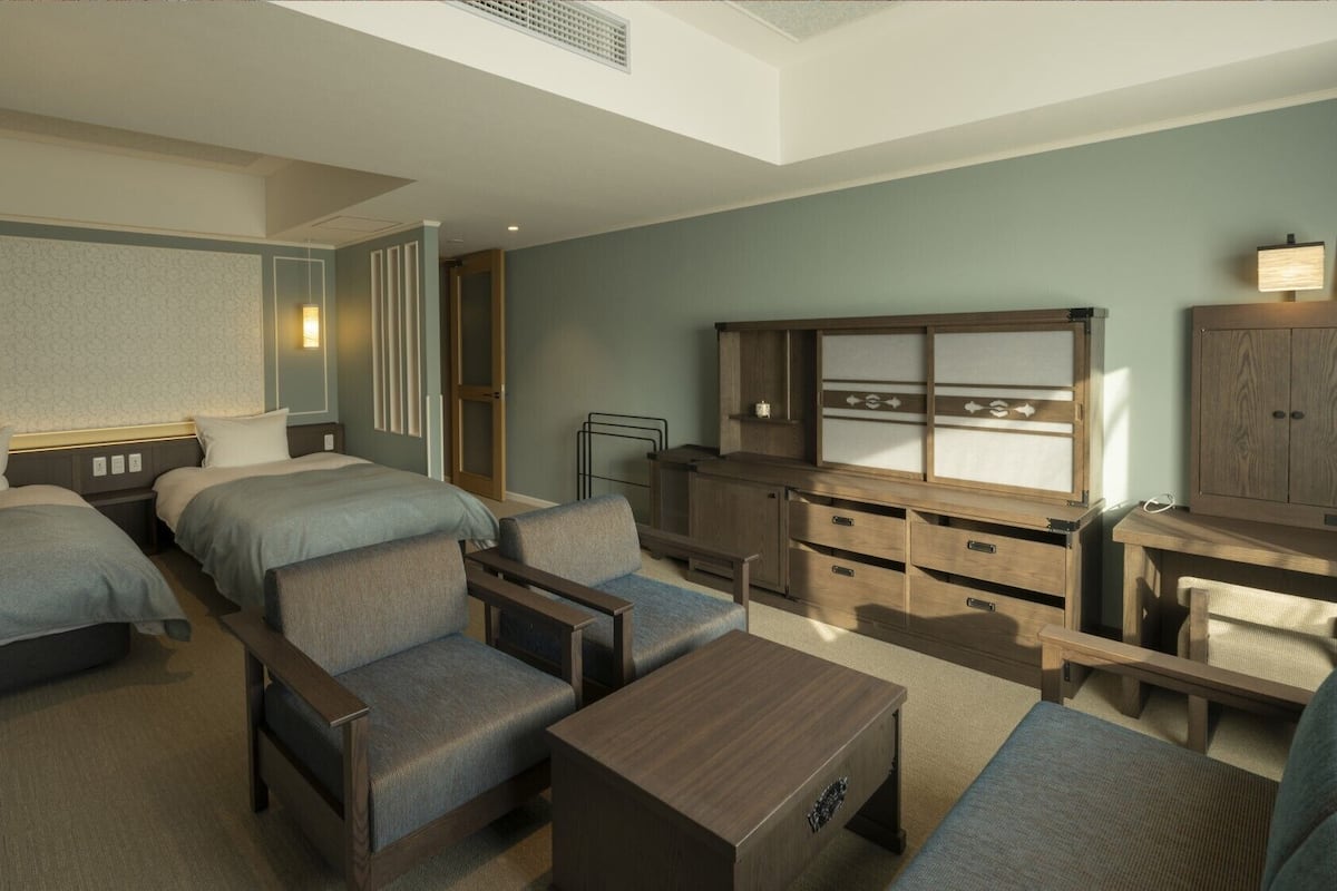 Habitación de hotel con dos camas, un escritorio, una silla, una mesita y un armario.