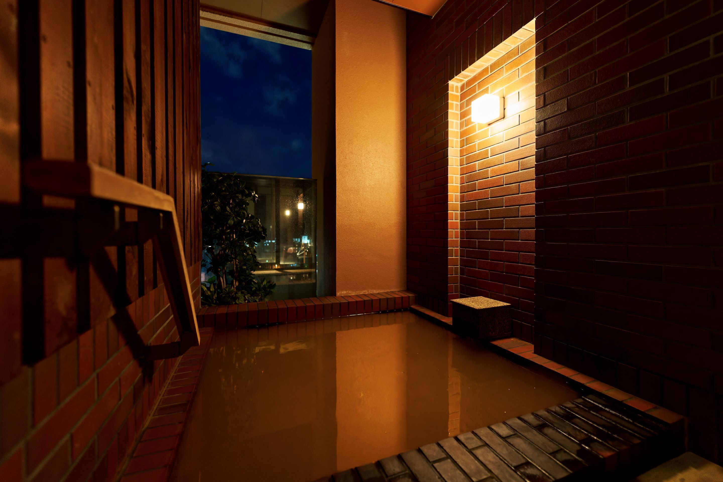 Vista nocturna de un edificio de ladrillo con un estanque reflectante y un banco de madera.