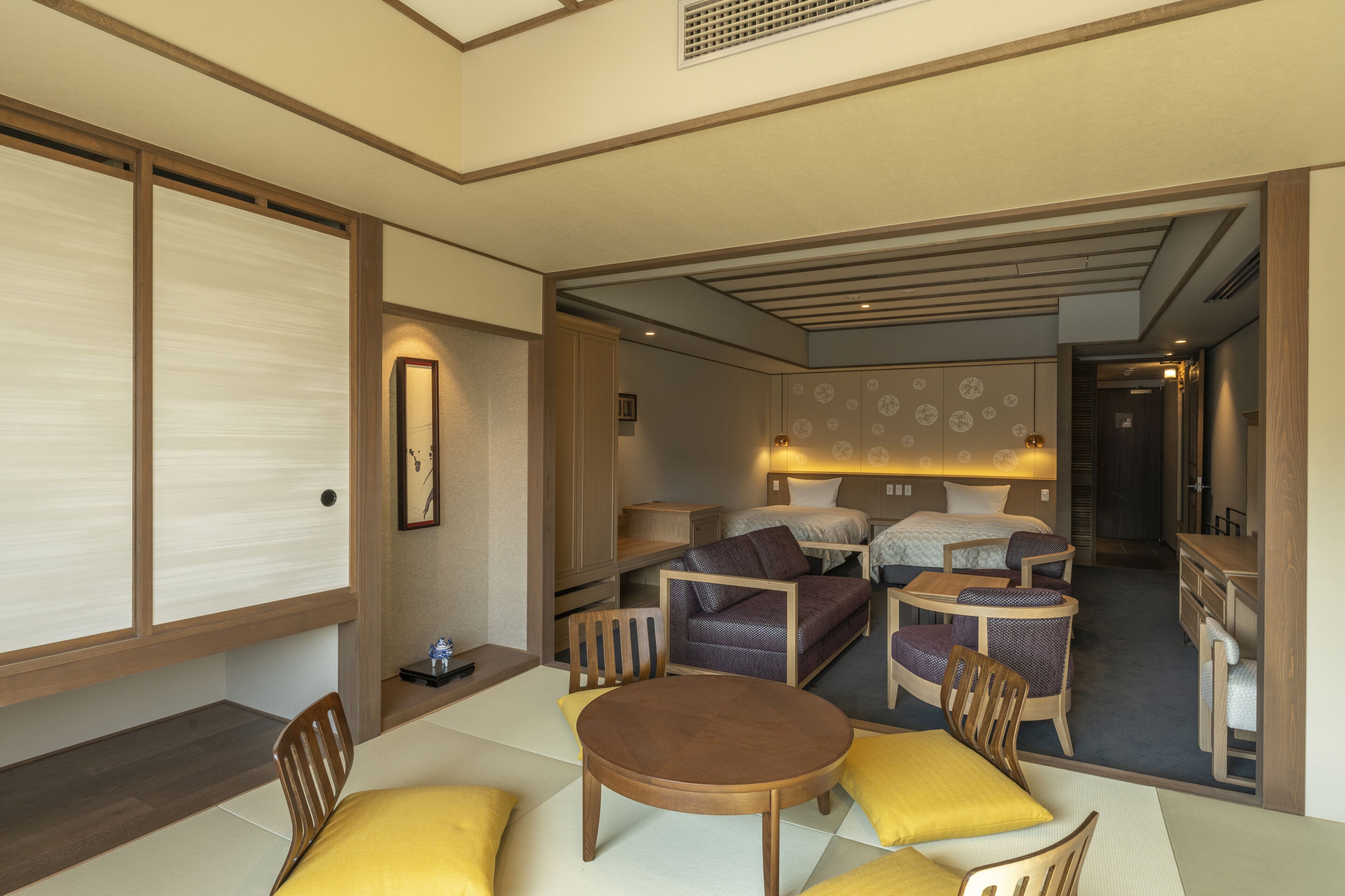 A compact hotel room with a bed, a sofa, a dining table, and a small kitchen area.