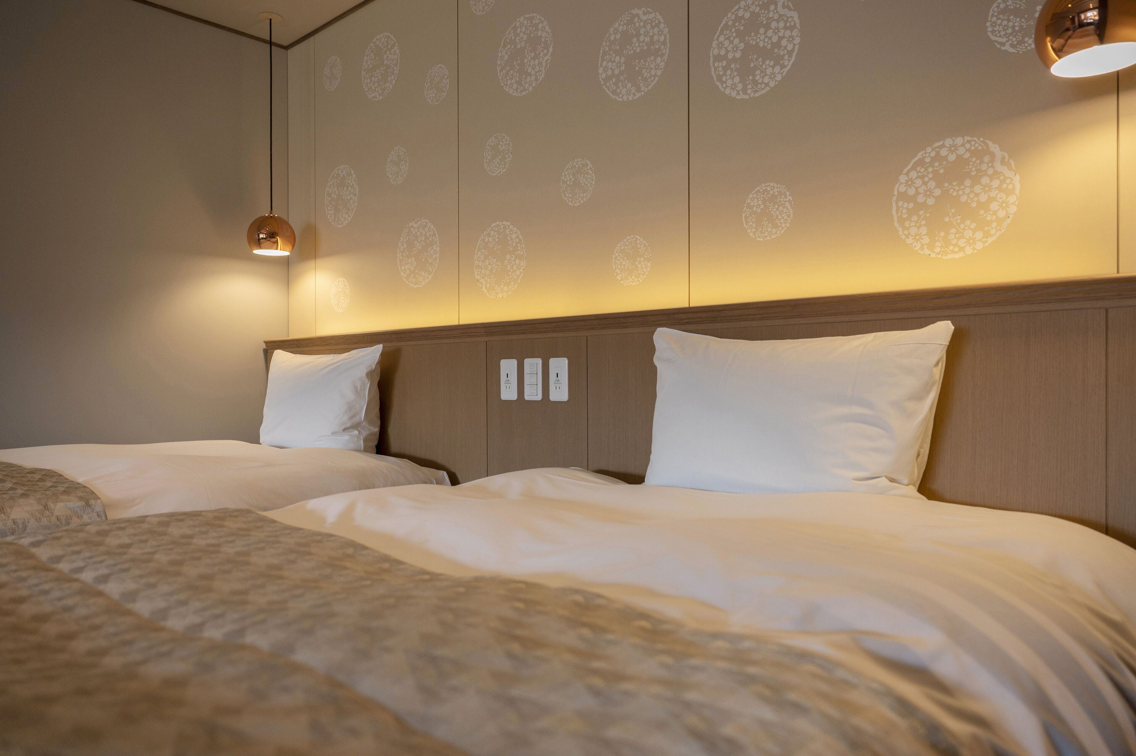 A hotel room with two beds, a wooden headboard, and a wall with circular floral patterns.