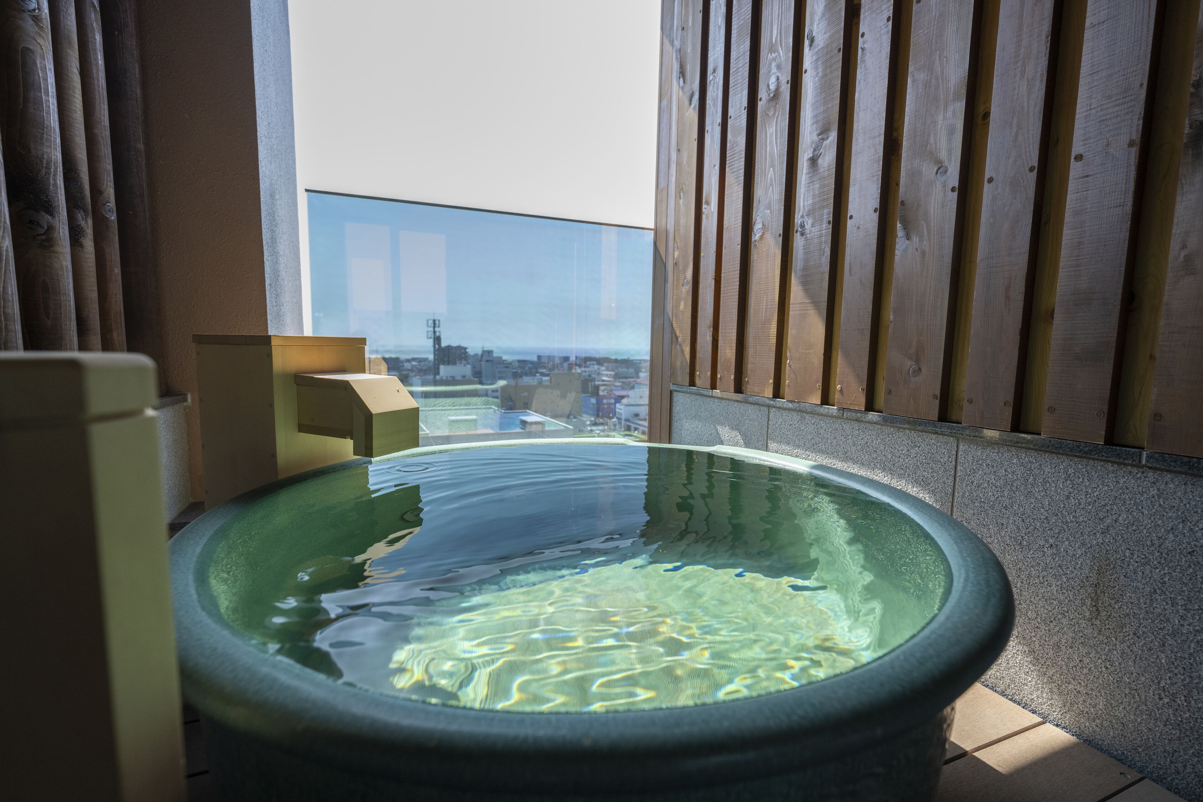 Un bain à remous avec vue sur la ville, des panneaux de bois et un mur en verre transparent.