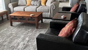 Un soggiorno con un divano grigio, una poltrona in pelle nera, un tavolino in legno e un tappeto decorato.
