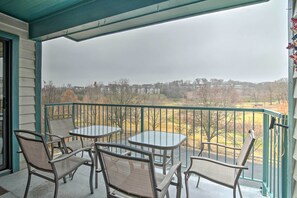 En balkon med to borde og fire stole, med udsigt over et boligområde med huse og træer.