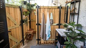 A wooden-fenced outdoor bathroom with a sink, hanging towels, and potted plants. - Romantic lakefront skoolie for 4: queen, twins, hot tub and private bathhouse (Granbury)