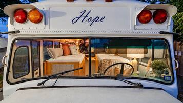 Un autobús reconvertit en casa rodant, amb un llit, una taula petita i una làmpada.