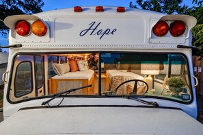 A bus converted into a mobile home with a bed, a small table, and a lamp. - Lakefront Skoolie for 4 with hot tub, bathhouse (Granbury)