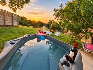 A hot tub with a fire feature, surrounded by a grassy yard and trees, with a sunset in the background. - Lakefront Skoolie for 4 with hot tub, bathhouse (Granbury)