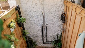 A narrow shower area with a stone wall, wooden benches, and potted plants. - Romantic lakefront skoolie for 4: queen, twins, hot tub and private bathhouse (Granbury)