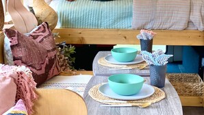 A cozy, well-lit room with a bed, a small table with a bowl and chopsticks, and a decorative plant. - Romantic lakefront skoolie for 4: queen, twins, hot tub and private bathhouse (Granbury)