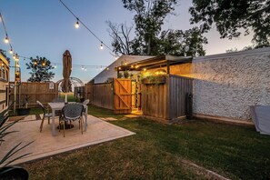 A backyard patio with a table and chairs, a wooden fence, and string lights. - Romantic lakefront skoolie for 4: queen, twins, hot tub and private bathhouse (Granbury)