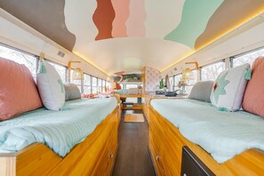 A cozy interior with two wooden beds, a central seating area, and large windows. - Romantic lakefront skoolie for 4: queen, twins, hot tub and private bathhouse (Granbury)