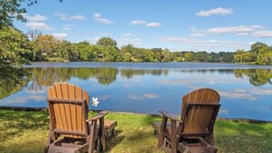 Two wooden Adirondack chairs facing a calm lake with a clear sky.