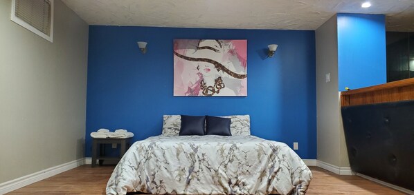 A bedroom with a blue wall, a bed with a floral bedspread, two wall-mounted lights, and a painting above the bed.
