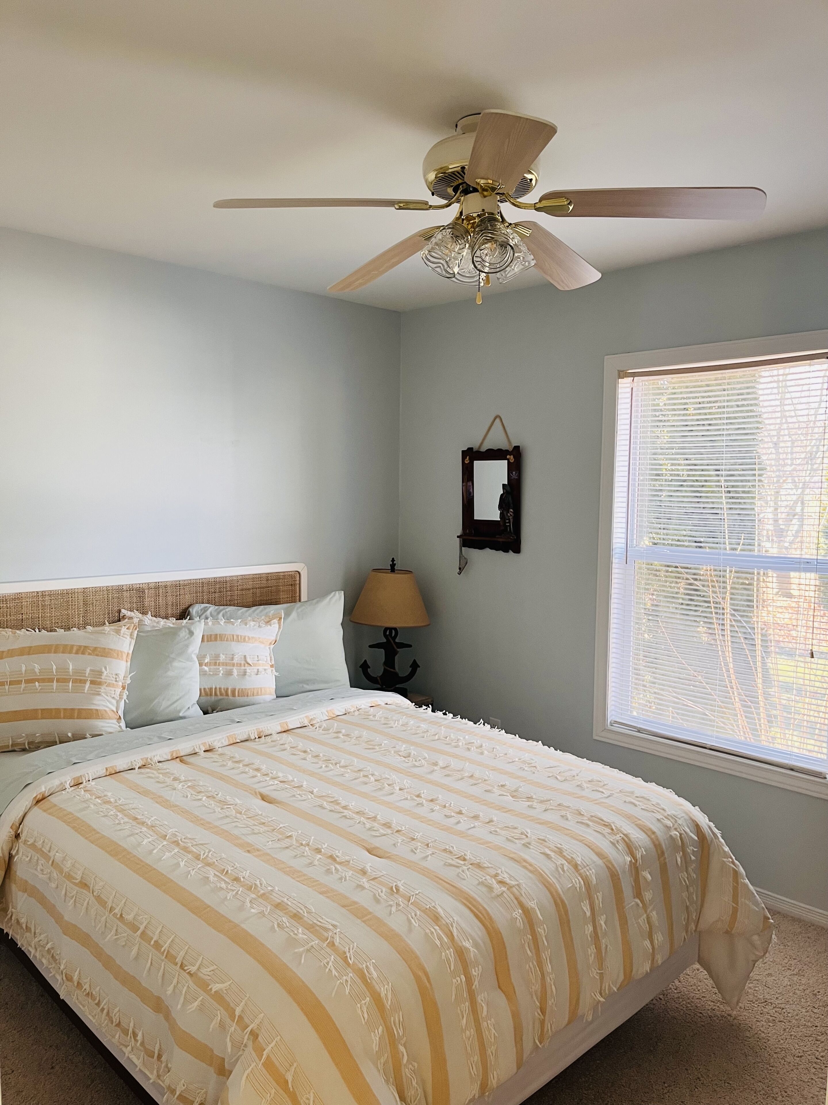 Ein Schlafzimmer mit Bett, Deckenventilator, Fenster mit Jalousien und Wandlampe.