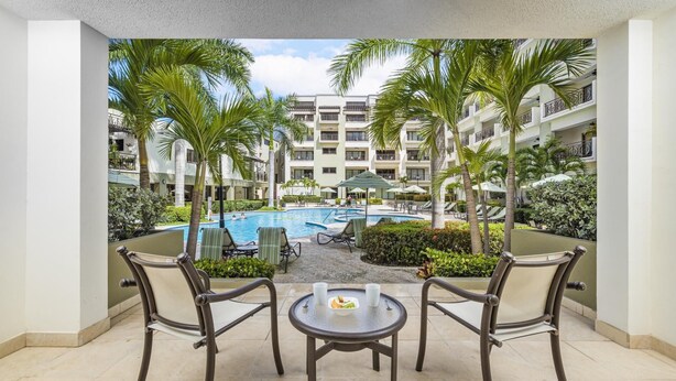 A poolside area with a view of a multi-story building, palm trees, and lounge chairs. - Beautiful One Bedroom Ground Level @ PalmAruba (Noord)
