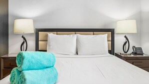 A hotel room with a large bed, two bedside lamps, a telephone, and a folded towel on the nightstand. - Beautiful One Bedroom Ground Level @ PalmAruba (Noord)