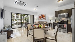 A modern kitchen with a dining area, a large window, and a view of a pool and buildings. - Beautiful One Bedroom Ground Level @ PalmAruba (Noord)