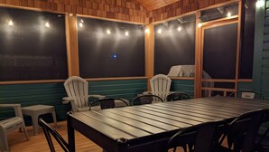 An outdoor patio with a metal table and chairs, surrounded by wooden walls and windows.
