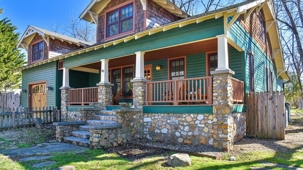 A two-story house with a stone foundation, a porch with wooden railings, and a wooden fence.