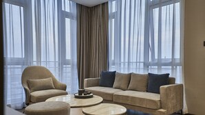 A modern living room with a sofa, armchair, and coffee table, large windows with sheer curtains, and a neutral color palette. - Qing Dao bu ke bu zhu hotel (Qingdao)