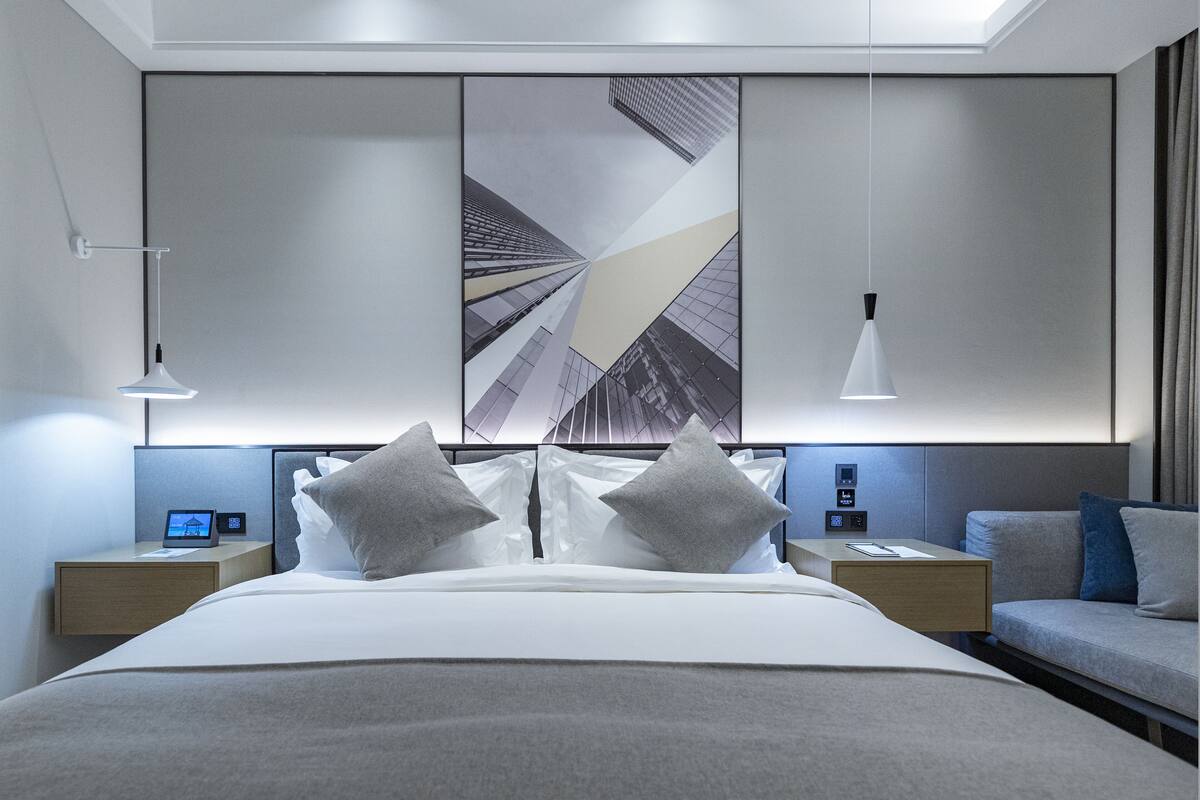 A modern hotel room with a large bed, bedside tables, a desk, and a large window.