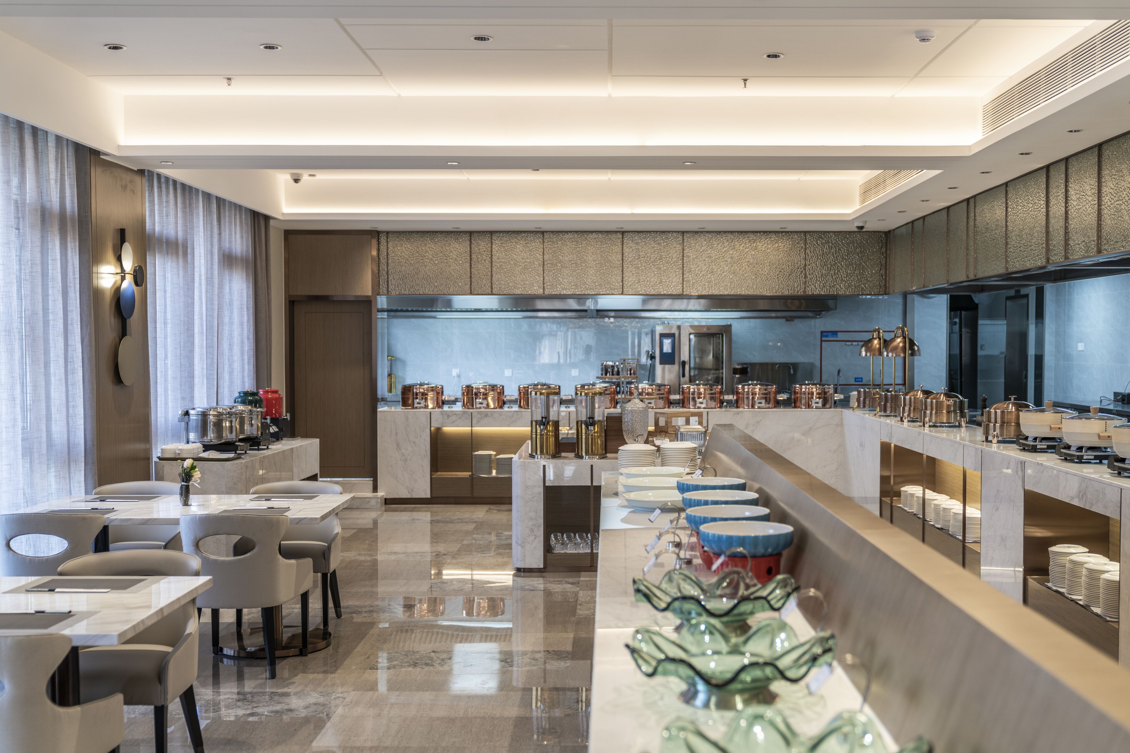 A modern hotel lobby with a long reception desk, seating area, and a kitchen in the background.