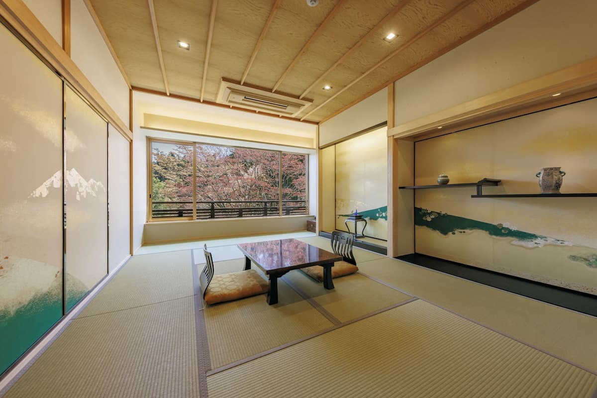 A traditional Japanese room with tatami flooring, a low table, and a view of autumn trees through a large window.