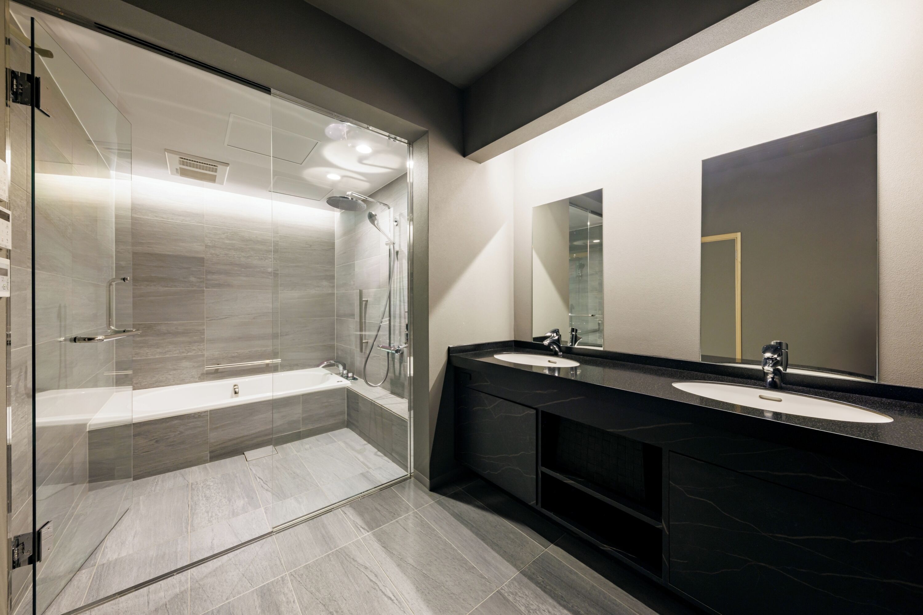 Ein modernes Badezimmer mit einer Glaskabine zur Dusche, einer großzügigen Badewanne und zwei Waschbecken mit dunklen Arbeitsplatten.