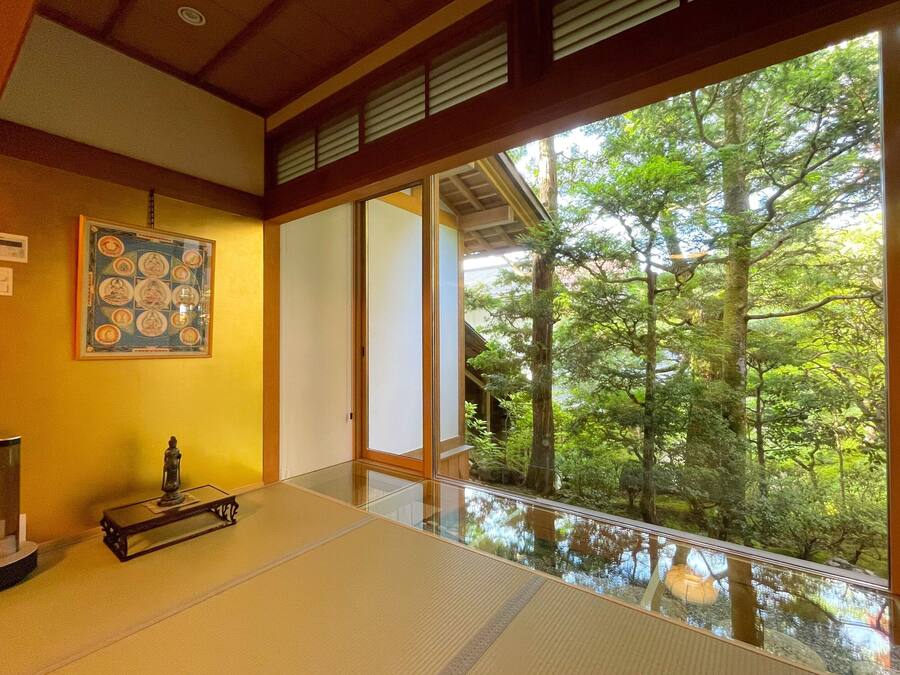 A tatami mat room with a large window overlooking a forest.