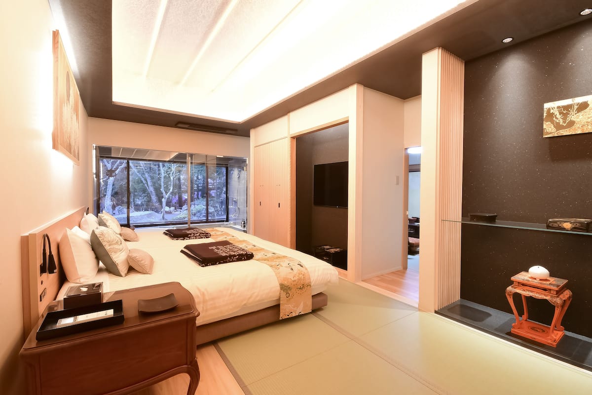 A modern bedroom with a large bed, bedside tables, a TV, and a view of the outdoors.