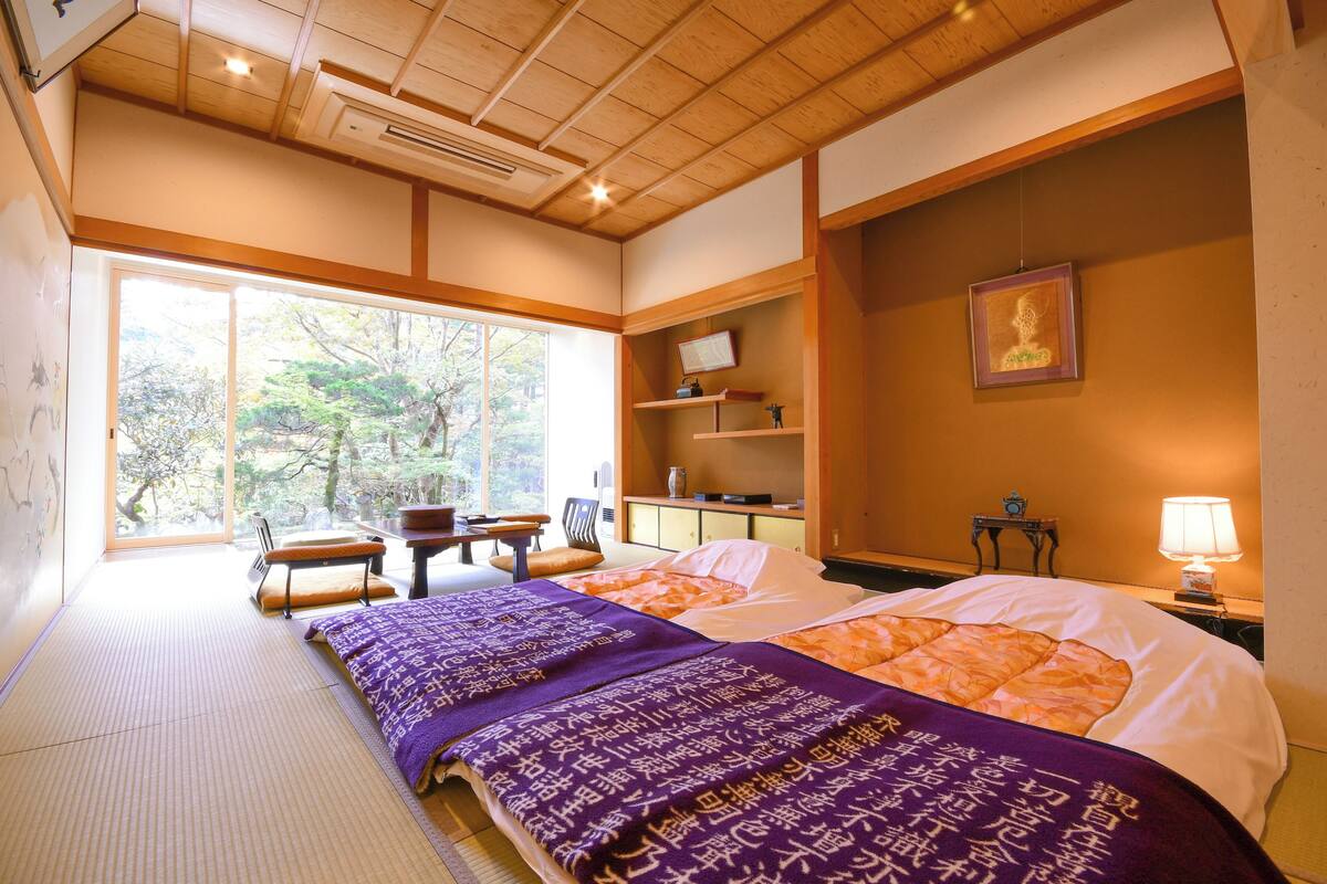 A traditional Japanese-style room with tatami flooring, a bed with a purple and orange bedding, a desk, and a chair.