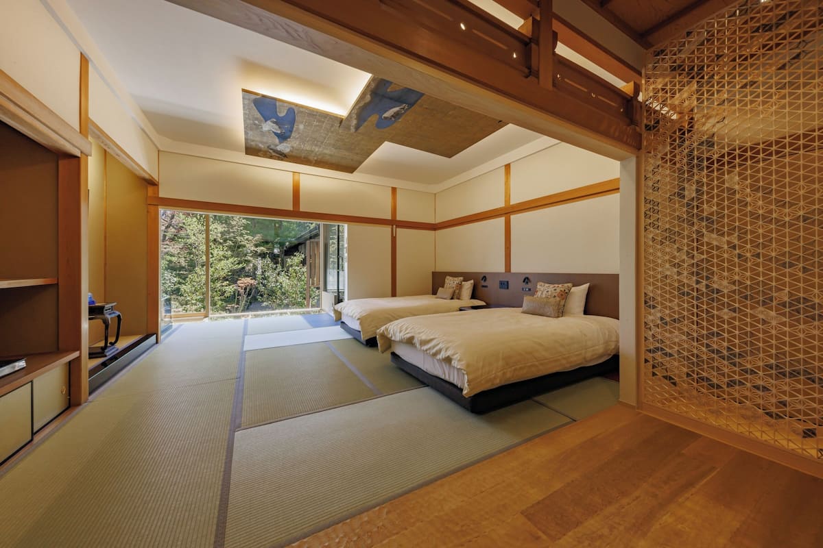 A traditional Japanese-style bedroom with tatami mats, a low wooden ceiling, and a view of greenery outside.