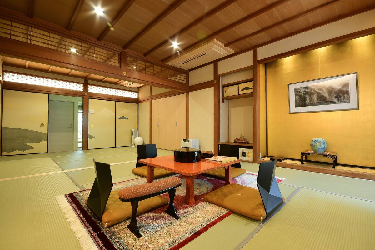 A traditional Japanese room with tatami flooring, a low table with cushions, and a framed picture on the wall.