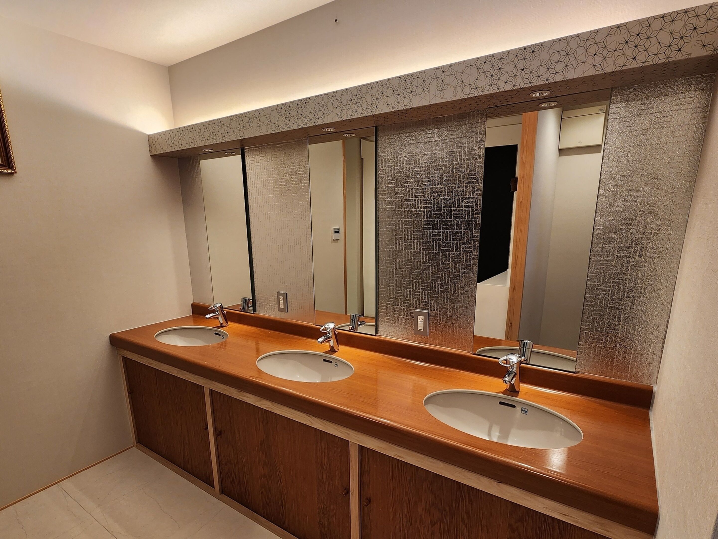 A bathroom with three sinks, wooden vanity, and a large mirror.