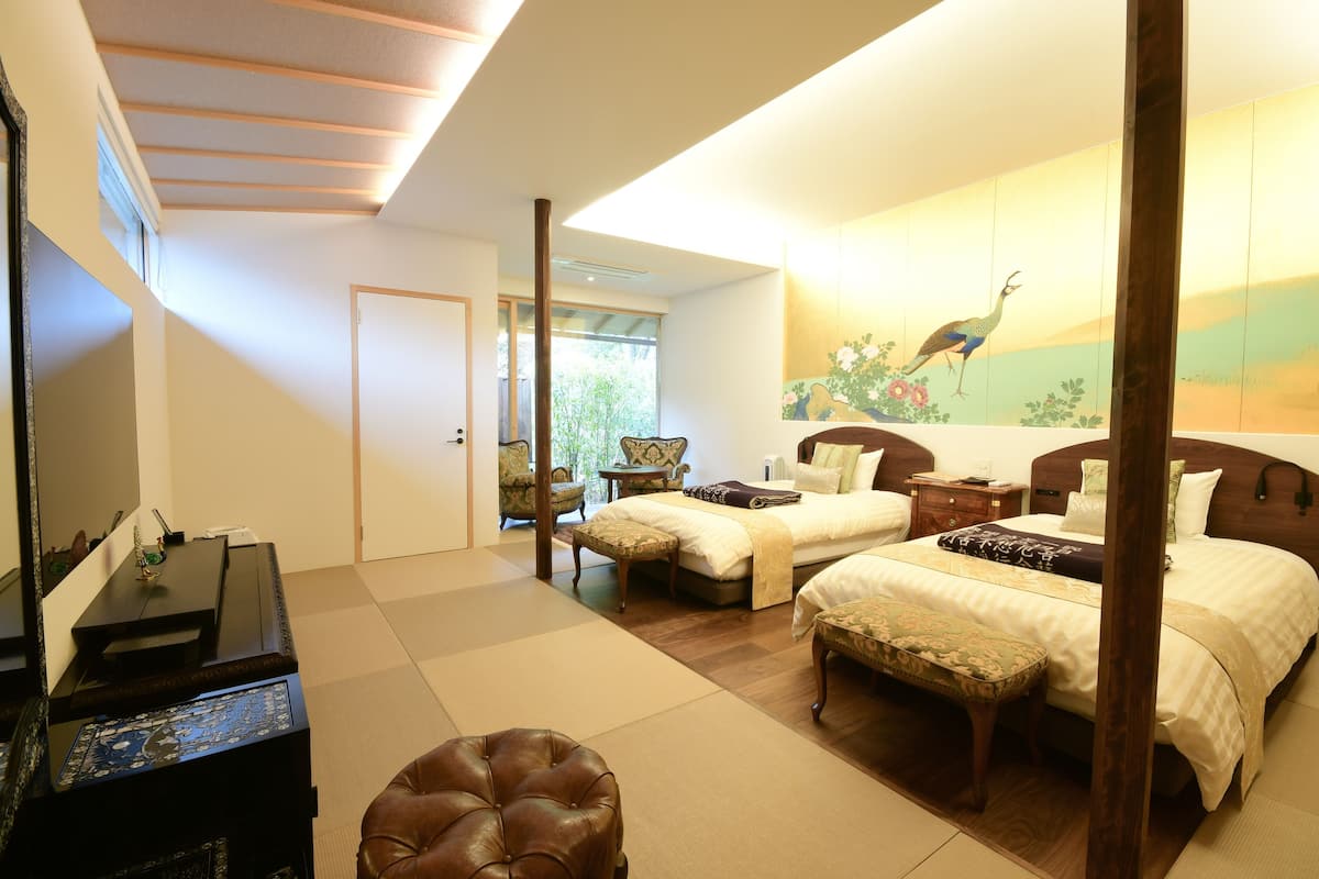 A hotel room with two beds, a desk, a chair, and a large painting of a peacock.
