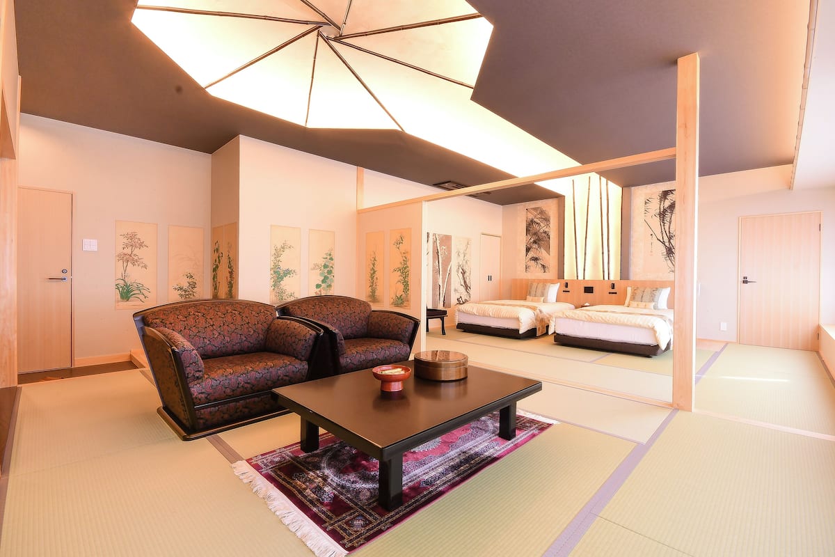 A traditional Japanese-style room with tatami flooring, a low wooden table, two patterned sofas, and a large ceiling fan.