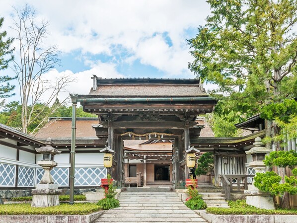 A traditional Japanese gate with a tiled roof, leading to a building with wooden walls and a tiled roof.