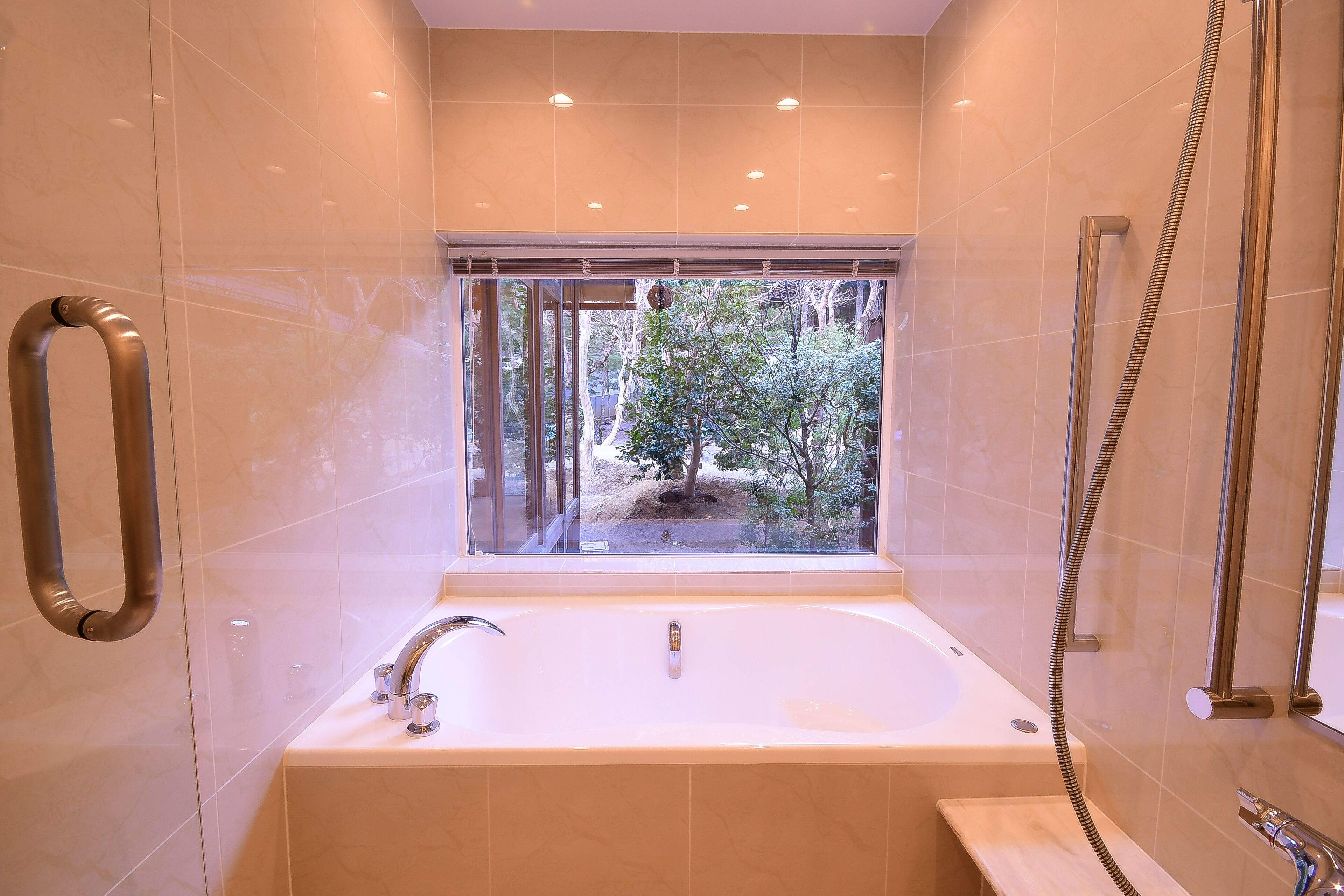 A modern bathroom with a large bathtub, a window with a view of trees, and a shower area.