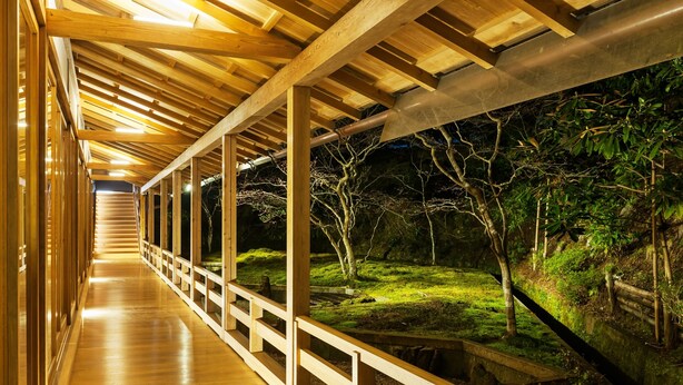 A wooden corridor with a view of a garden at night.