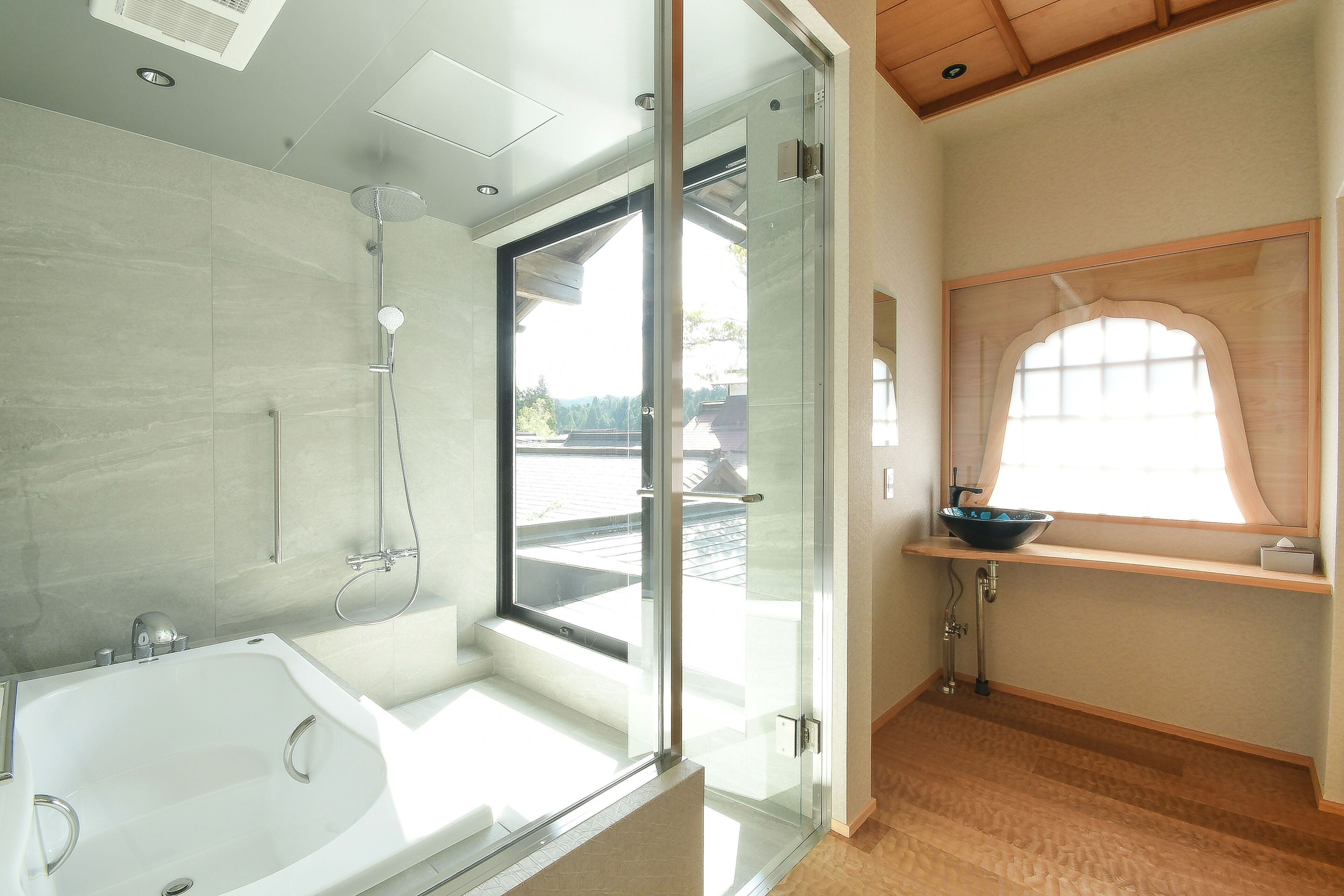 Un baño moderno con ducha envuelta en vidrio, una bañera blanca y un ventanal que aporta luz natural.