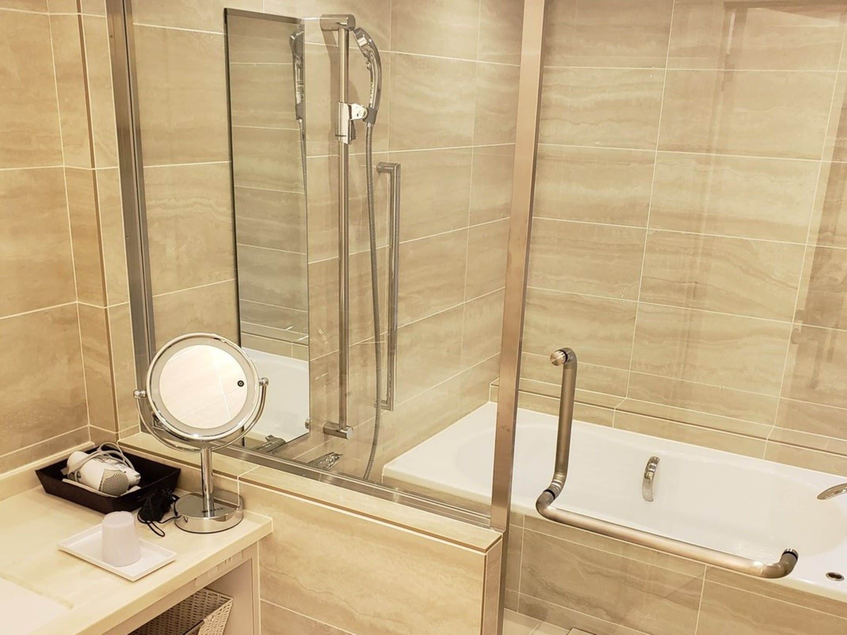 A bathroom with a glass-enclosed shower, a standalone bathtub, and a vanity with a mirror and toiletries.