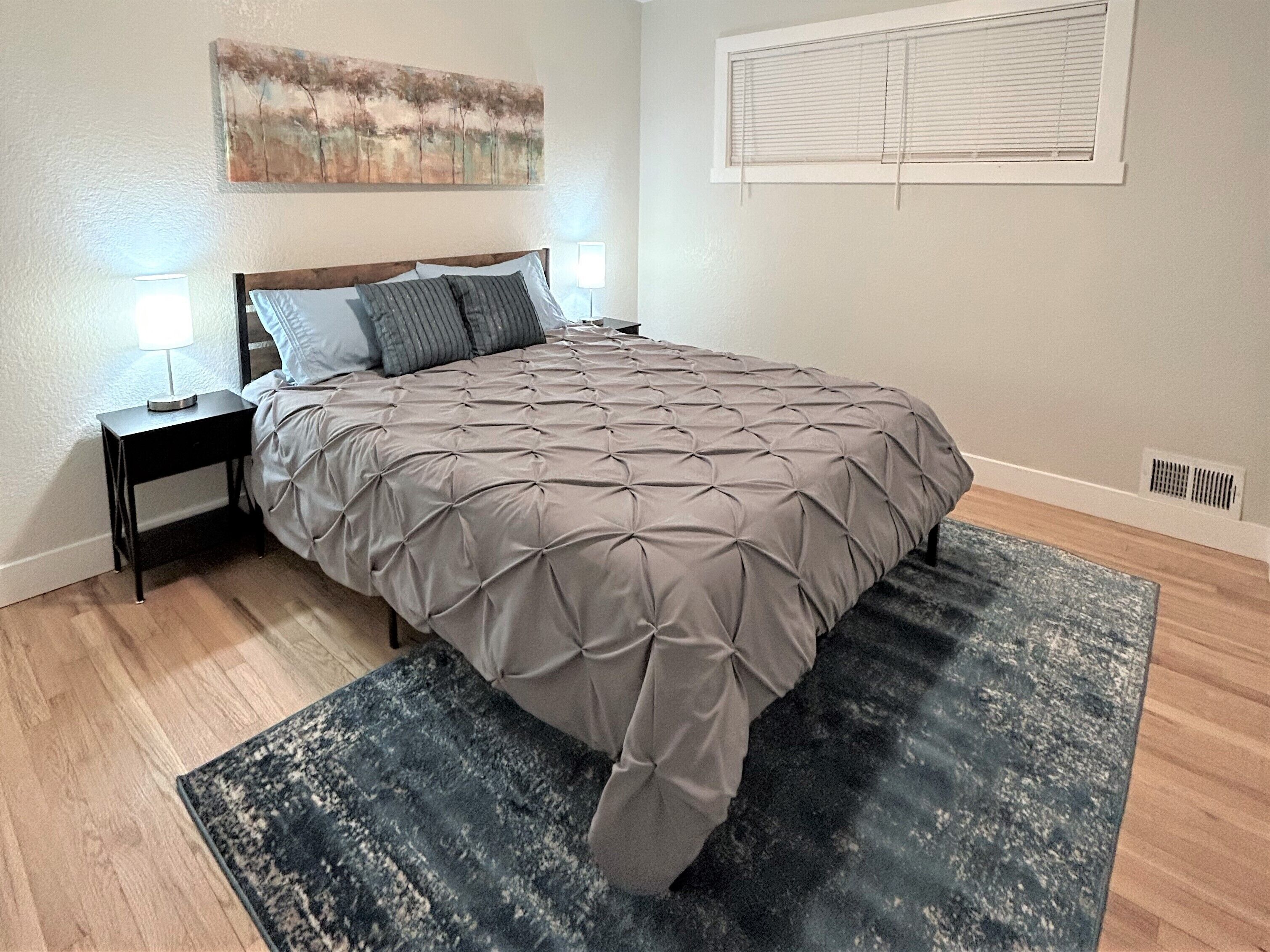 Quarto com cama, mesas de cabeceira, um quadro e janela com persianas.