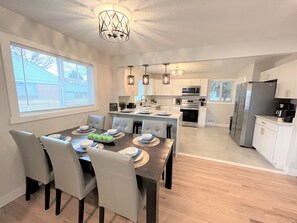 Una cocina moderna con armarios blancos, electrodomésticos de acero inoxidable y una zona de comedor con mesa y sillas de madera.