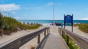 A wooden boardwalk leading to a beach with a safety sign and a lifeguard tower. - EXQUISITE BEACH HAVEN! PERFECT ROMANTIC GETAWAY! DOG FRIENDLY! (Destin)