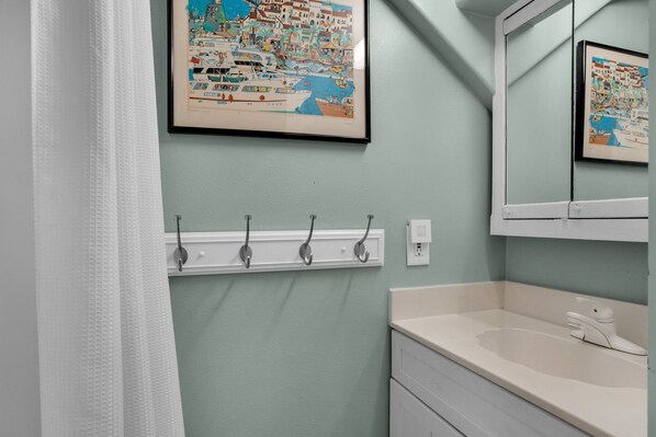 A bathroom with a light green wall, a white sink, and a mirror. There are four hooks on the wall, and a framed picture above the sink. - EXQUISITE BEACH HAVEN! PERFECT ROMANTIC GETAWAY! DOG FRIENDLY! (Destin)