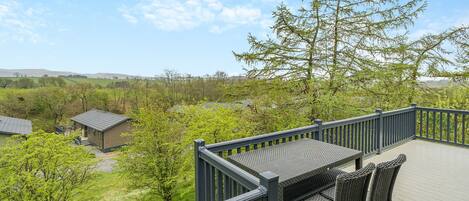 A deck with wicker furniture, a view of a green landscape, and a building in the background.