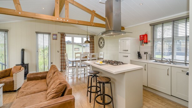 A modern kitchen with a central island, wooden beams, a built-in stove, and a large window.